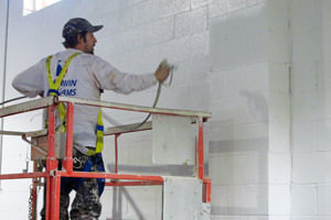 painter spray painting an industrial building wall