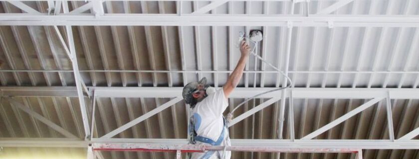 industrial painter spray painting a metal ceiling