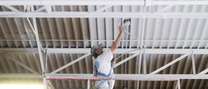 industrial painter spray painting a metal ceiling