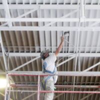 industrial painter spray painting a metal ceiling