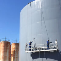 industrial painters spray painting a steel storage tank